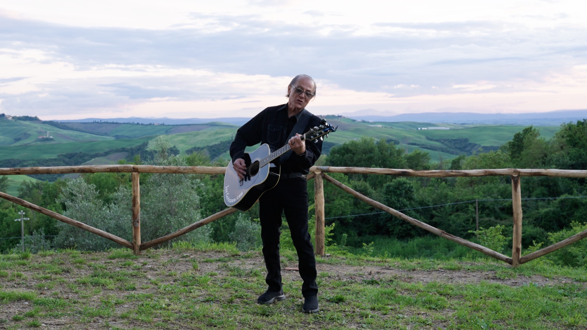 Joe Cerisano playing guitar against the Tuscan hills